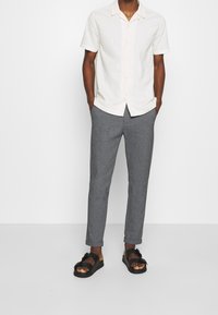 Koszula na krótki rękaw w jasnym kremowym kolorze, szare dopasowane spodnie i czarne sandały z paskami i kokardą. Prosty i nowoczesny design.