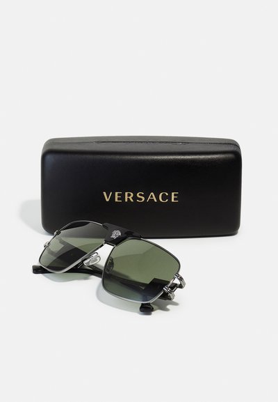 Lunettes de soleil Versace avec verres verts, accessoires en argent et monture noire. Comprend un étui noir avec "VERSACE" en lettres dorées.