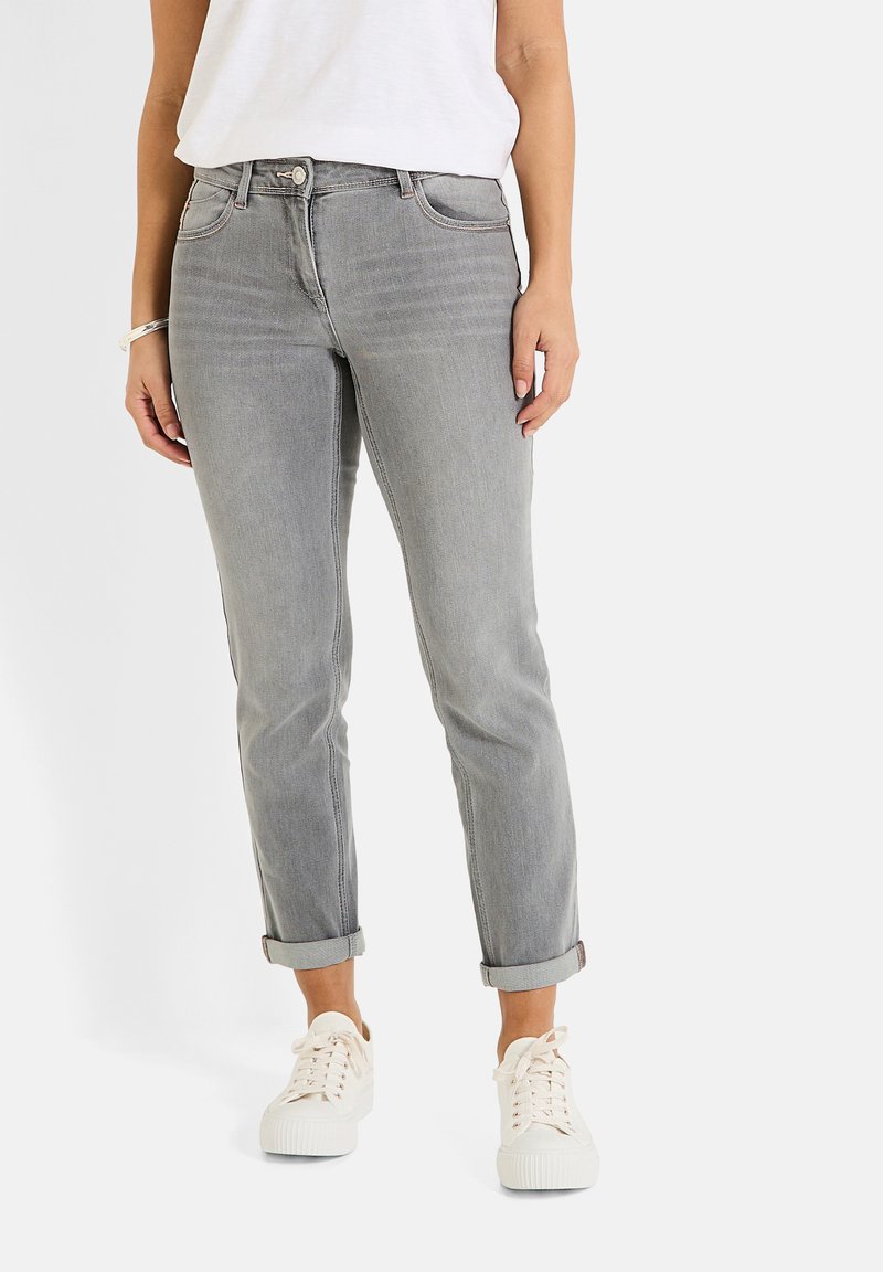 Jeans de mezclilla gris con un diseño ajustado, puños doblados, bolsillos frontales y cierre de botón metálico, combinados con zapatillas blancas.