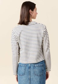 Maglietta a maniche lunghe a righe in crema e blu navy, con collo rotondo e taglio corto. Abbinata a una gonna di jeans con due tasche posteriori.