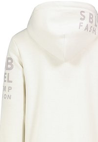 Helles cremefarbens Hoodie mit Kapuze und Zugband, sichtbaren Nähten und bedruckten Textakzenten in Hellgrau auf dem Ärmel und dem Rücken.