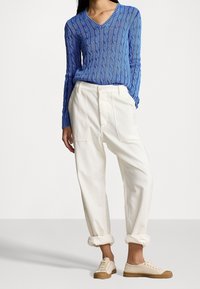 Blå kabelstickad v-ringad tröja, vita avslappnade byxor med sidofickor, och beige låga sneakers med gummisula.