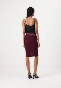 Schwarzes Satin-Camisole kombiniert mit einem burgunderfarbenen Bleistiftrock aus Spitze mit floralem Muster und einem schmalen Taillenbund. Getragen mit schwarzen High Heels Sandalen.