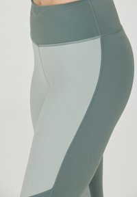 Högmidjade leggings i dämpad grön färg med kontrasterande ljusgröna paneler. Tillverkade av stretchigt material och har platta sömmar för extra komfort.