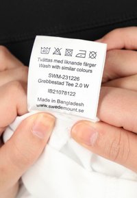 Hvidt stofmærke med vaskeanvisninger, produktkode SWM-231226, Grebbestad Tee 2.0 W, produceret i Bangladesh, Swedemount hjemmeside.