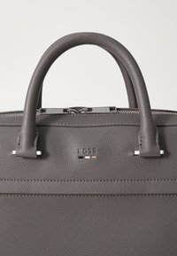 Dunkelgraue Lederhandtasche mit strukturiertem Finish, doppelten Griffen und silberfarbener Hardware mit geprägtem Logo und dezenten Farbakzenten.