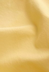 Tissu jaune doux avec une texture lisse et des plis délicats créant des motifs de lumière et d'ombre.