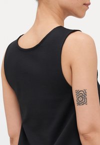 Juodas be rankovių viršus su apvalia iškirpte ir lygiu paviršiumi, demonstruojantis gėlių tatuiruotę ant išorinės rankos.