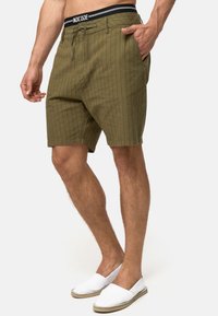 Khaki shorts med vertikale striber; lavet af letvægtsstof, med sidelommer og en sort snørelinning. Hvide slipsko.