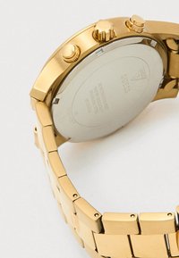 Relógio de pulso em metal dourado exibindo a parte de trás com a marca gravada, resistência à água, detalhes em aço inoxidável e uma bracelete com elos ligados.
