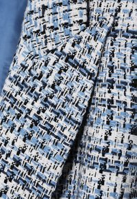Textil tejido con un patrón de hilos azules, blancos y negros con un acabado texturizado, que presenta un diseño de tejido diagonal.