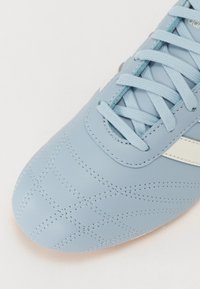 Ljusblå lädersneakers med texturerad ovandel och sydda mönster samt vita accenter. Snörning i matchande blått, platt och flätad design.