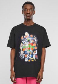 Sort bomulds T-shirt med et farverigt "Space Jam" grafik, der viser tegneseriefigurer, basketballer og en kosmisk baggrund. Korte ærmer.