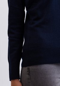 Navyblå stickad tröja med ribbade ärmslut och fåll, med en mjuk yta och en figurvänlig design, matchad med grå byxor.