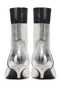 Botines plateados con un acabado metálico brillante, que presentan una parte superior de tela negra y un tacón en forma de cono. Textura suave y diseño elegante.