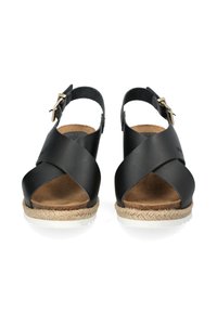 Schwarze Ledersandalen mit einem Kreuzmuster und Knöchelriemen, die eine mit Jute umwickelte Sohle und eine hellfarbene Gummisohle haben.