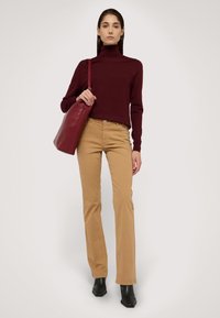 Burgundský rolák, béžové široké kalhoty, černé kotníkové boty a červená kožená taška. Hladké textury a dobře padnoucí střih.