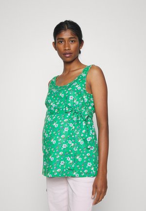 Blusa de maternidade verde floral com um corte solto, decote arredondado e detalhe em laço lateral. Apresenta pequenas flores brancas e azuis por toda a peça.