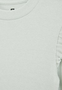 Svetlo zelena rebrasta bluza z dolgimi rokavi in okroglim izrezom, okrašena z nabranimi detajli na ramenih, izdelana iz mehkega, teksturiranega blaga.