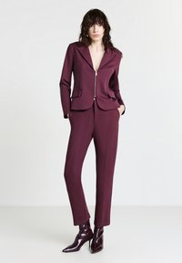 Completo bordeaux con giacca aderente a zip e due tasche, abbinato a pantaloni affusolati e stivaletti a punta con tacco alto.