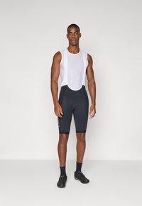 Cuissards de cyclisme noirs avec un haut en maille blanche. Les cuissards sont dotés de grippe-jambes et d'accents latéraux, conçus pour le confort et la performance.