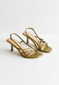 Sandales à talons hauts en cuir verni vert olive avec un orteil carré, présentant plusieurs fines lanières et des boucles en ton doré comme accents.