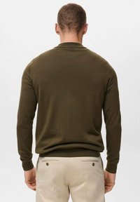 Olive zelena jopica s okruglim izrezom in rebrastimi manšetami. Pletena tkanina, oprijet kroj, opažena s hrbtne strani, se lepo ujema s svetlim hlačami.