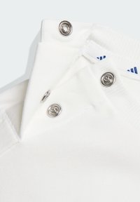 Biały bawełniany ubranie z zatrzaskami, posiadające prążkowaną fakturę i złożony kołnierz. Widoczne przeszycia wzdłuż krawędzi.