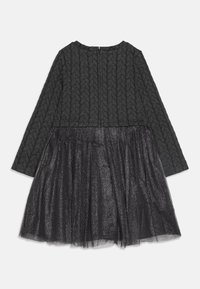 Abito nero con un top strutturato e una gonna in tulle a strati e luccicante. Maniche lunghe e scollo rotondo. Chiusura con zip sul retro.