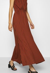 Hnědo pruhované maxi šaty s přiléhavým pasem, splývavou sukní a krátkými rukávy. Nosené s černými sandály na blokovém podpatku.