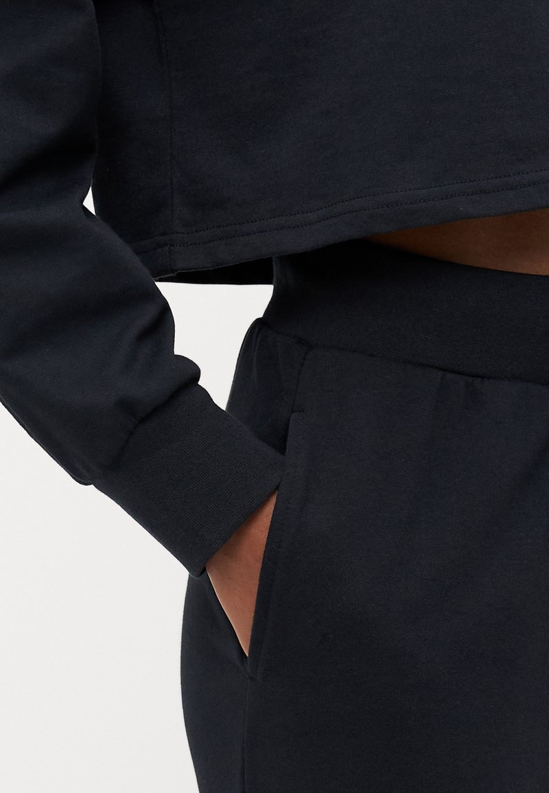 Felpa nera a vita corta con maniche lunghe e polsini a coste, abbinata a pantaloni a vita alta coordinati dotati di tasche laterali.