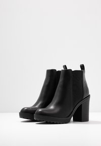 Bottines noires avec une finition en cuir lisse, panneau latéral texturé et talon épais. Présente un bout rond et des accents à motifs.