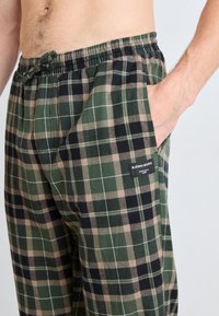 Rutiga pyjamasbyxor i grönt, svart och beige med elastisk midja, sidofickor och en logotyp framtill.