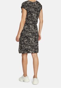 Svart och krämmönstrad klänning med korta ärmar och åtstramad midja, matchad med vita sneakers. Slät tygtextur.