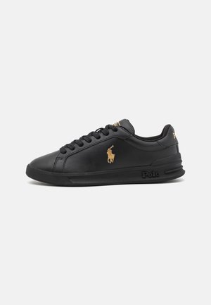 Baskets basses noires avec lacets noirs, logo Polo doré sur le côté, et marquage en relief "Polo" sur la semelle, sur fond blanc.