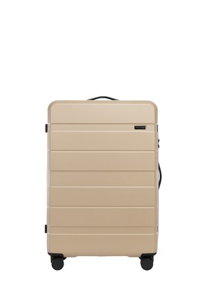 Valise rigide beige avec des rainures horizontales, accents noirs, poignée latérale et quatre roues pour un déplacement fluide et facile.