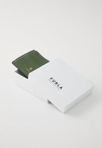 Green textured cardholder partially inside a white box, featuring a gold logo and four card slots, with a zip pocket on top.