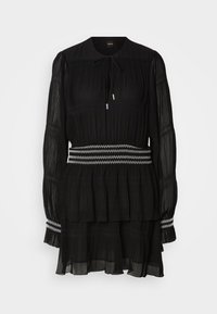 Sort langærmet plisseret kjole med hvid zigzagkant ved talje og manchetter, bindesnøre ved halsen og lagdelt chiffon-nederdel.