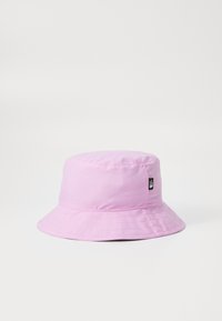 Rosa bomullshatt i bucket-modell med bred skärm, sömda detaljer och en liten svart logotyp-patch på sidan. Slät textur och strukturerad form.