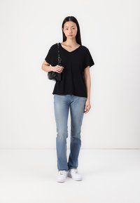 Top negro de manga corta y escote en V combinado con jeans rectos de mezclilla azul claro y zapatillas blancas, complementado con un pequeño bolso negro.