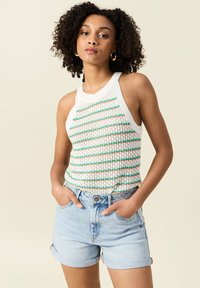 Gehaakte haltertop met een witte basis, gekenmerkt door meerkleurige strepen in groen en perzik. Gecombineerd met lichtblauwe denimshorts.