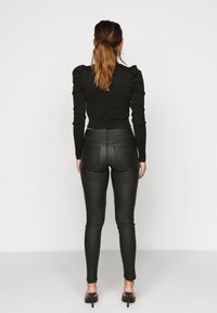 Top negro de manga larga con hombros abullonados, combinado con pantalones ajustados de cuero negro y sandalias de tacón alto negras, visto desde la parte posterior.