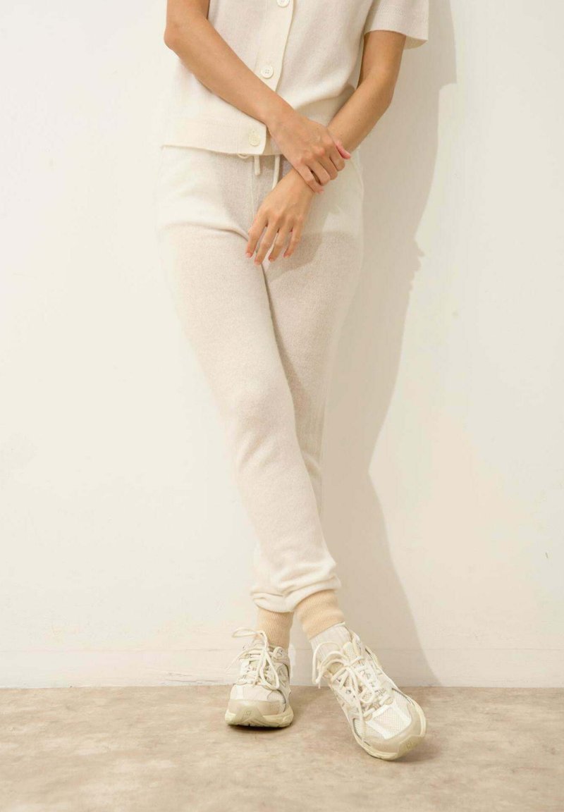 Mjuk, krämfärgad stickad tröja och matchande joggers med elastiska ärmar. Skorna har neutrala sneakers med mesh-detaljer.