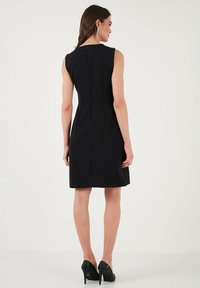 Black sleeveless dress with a fitted bodice, smooth texture, knee-length hem, and zip closure at the back. Worn with black high heels.