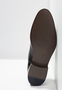 Zwarte leren dressshoe met een gladde afwerking, puntige neus en platte rubberen zool met een gegraveerd logo en maat 41.
