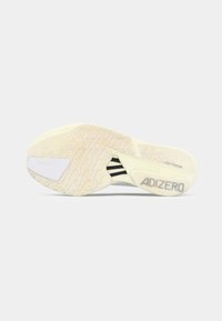 Semelle d'une chaussure de sport beige clair avec une texture antidérapante, logo Continental, rayures noires et le marquage "ADIZERO" au niveau du talon.