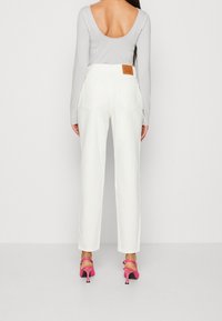 White high-waisted trousers with back pockets, paired with a light gray long-sleeve top and pink heeled sandals. Leather accent at the waist.
