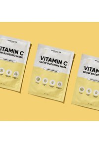 Paquets de masque éclatant à la vitamine C avec un emballage jaune et blanc, présentant des icônes des ingrédients. Trois paquets sur un fond jaune.