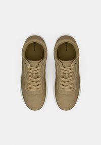 Et par beige snøre-sneakers med hvite såler, sett ovenfra på en enkel hvit bakgrunn.