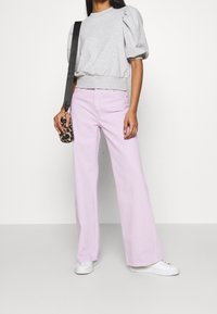 Felpa grigia con maniche a sbuffo e jeans larghi color lavanda. Modella che indossa sneaker bianche, tenendo in mano una custodia per telefono con stampa leopardata.
